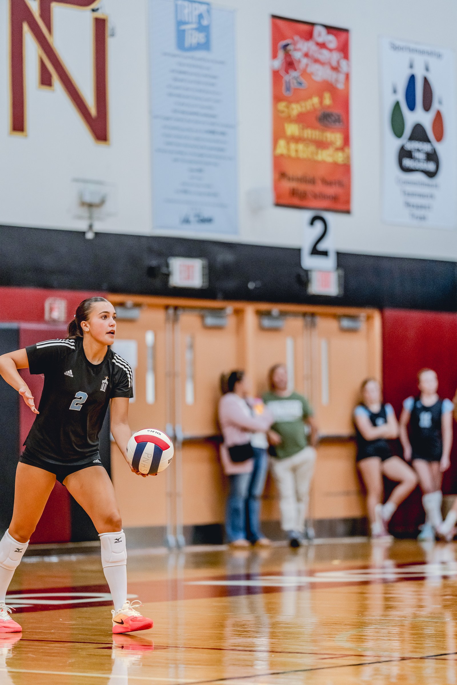 A player in a black jersey with white stripes and number 2 prepares to pass a volleyball during a game.