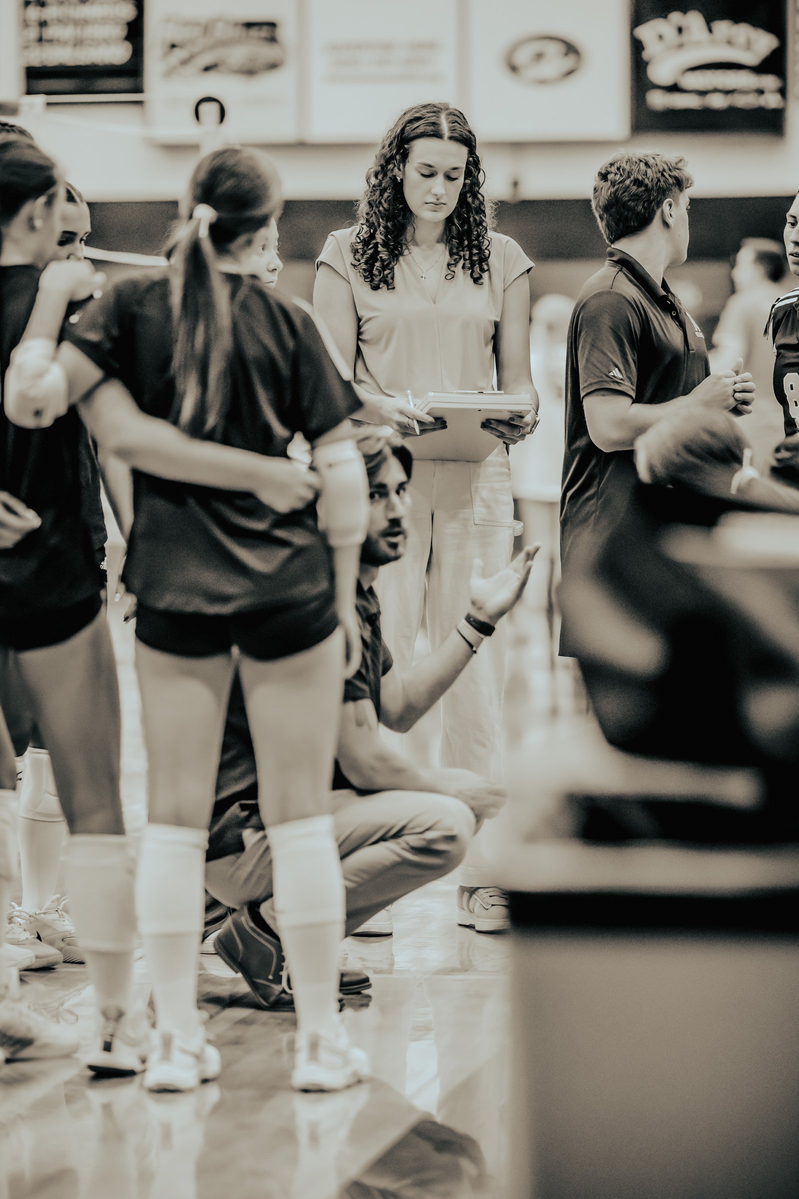 Players in black and white uniforms huddle with coaches on the court during a volleyball game.