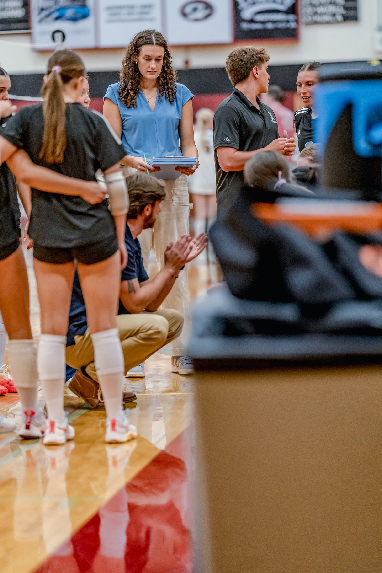 Players in black and blue uniforms huddle on the court during a volleyball game.