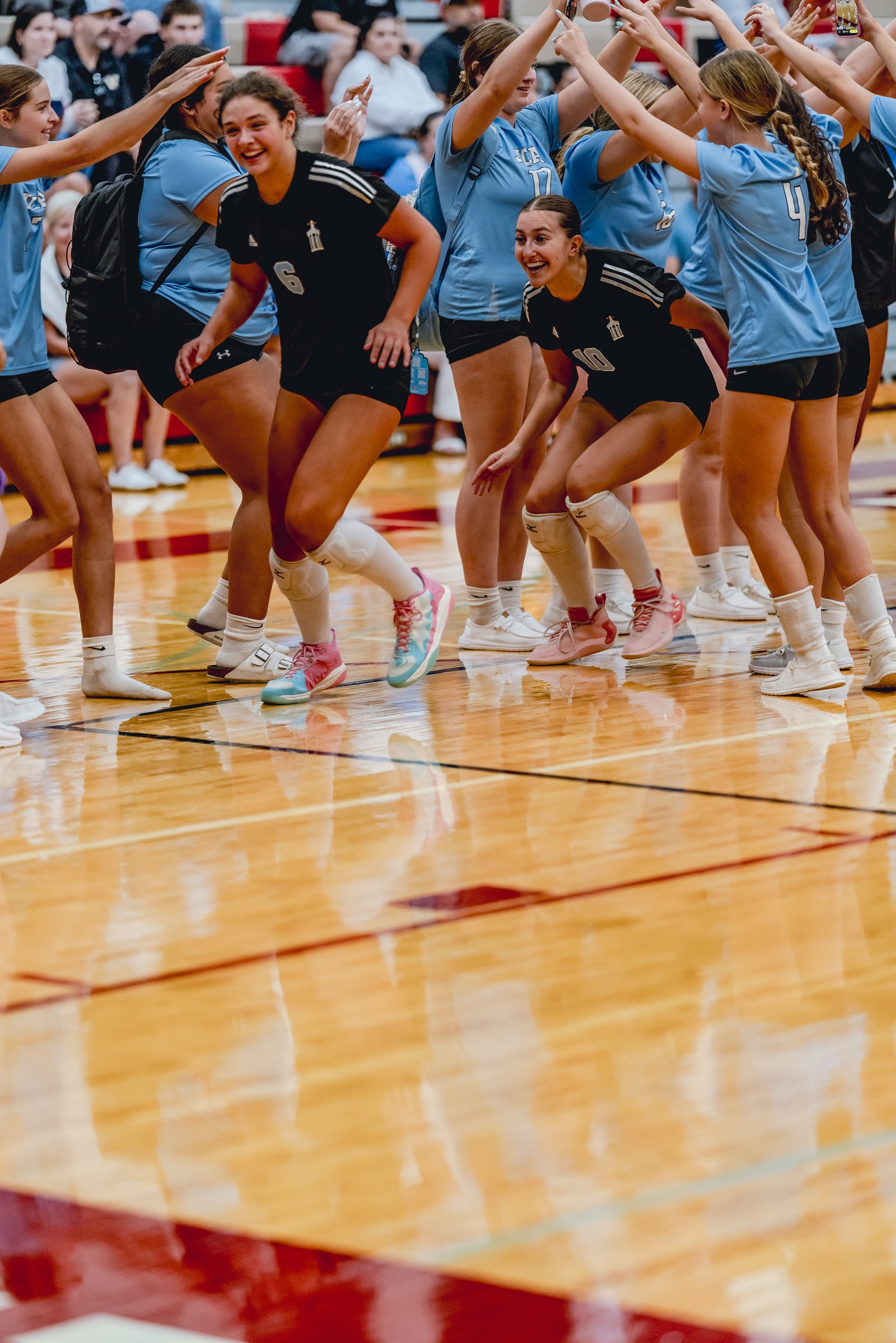 Players in black and blue jerseys celebrate on the court during a volleyball game.