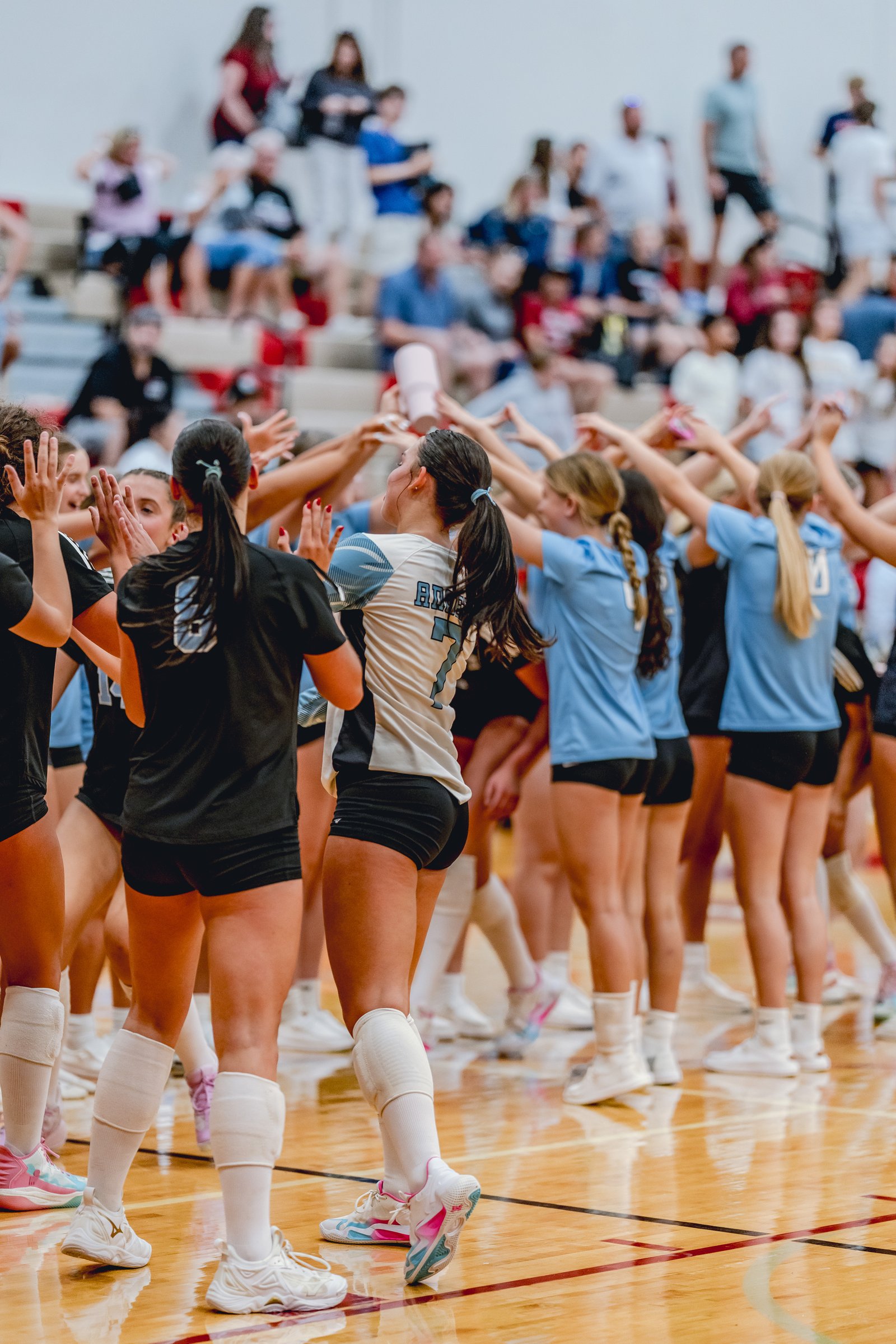 Players in black and light blue jerseys celebrate on the court, with spectators in the background.