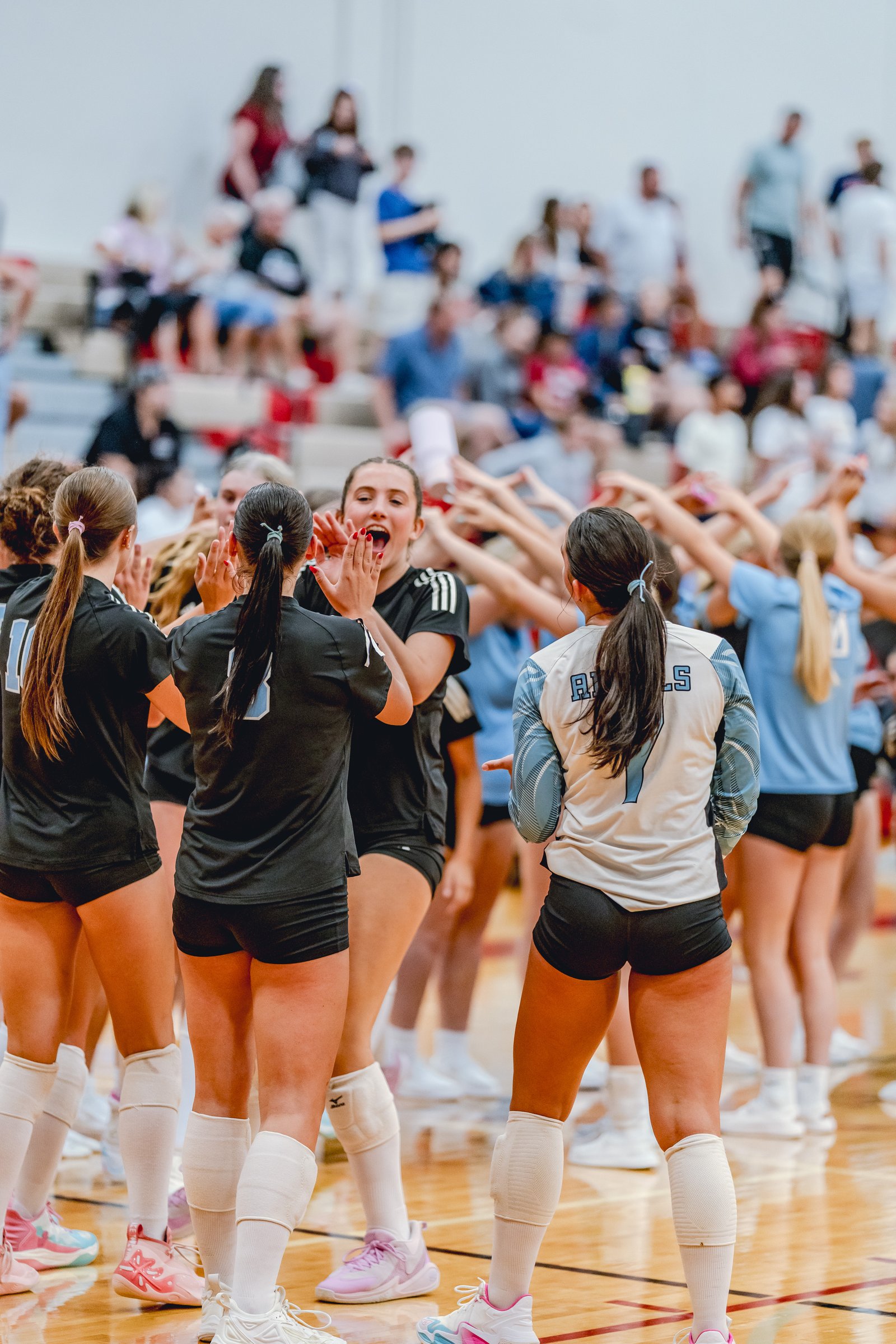 Players in black and light blue jerseys huddle together on the court, with one player in black shouting.