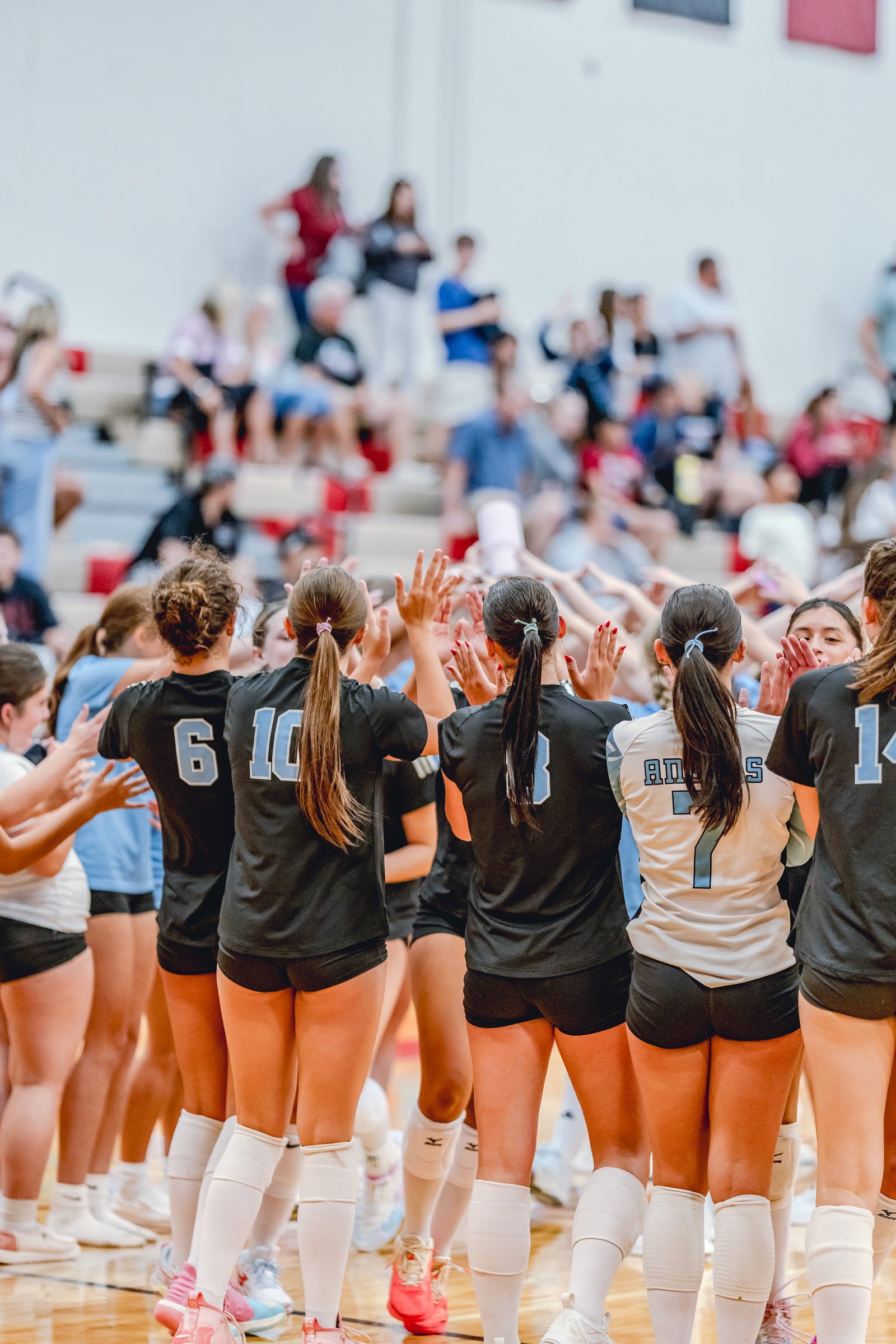 Players in black and white jerseys with blue numbers huddle with hands raised, some wearing knee pads and white socks.