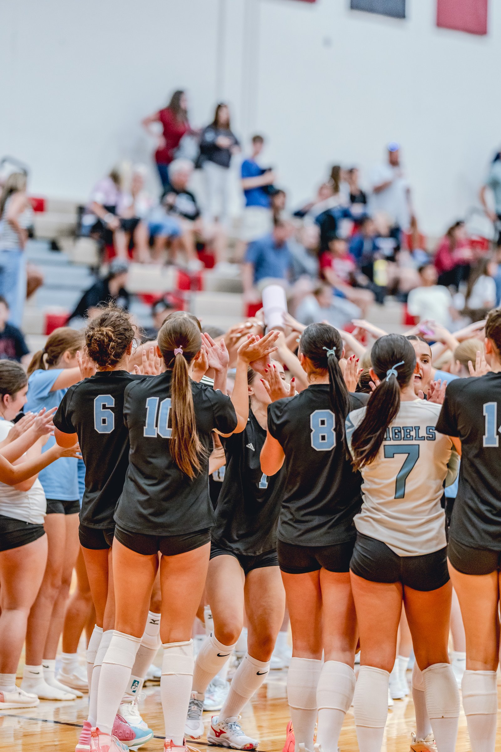 Players in black and white jerseys huddle together, clapping hands in a gym with spectators in the background.