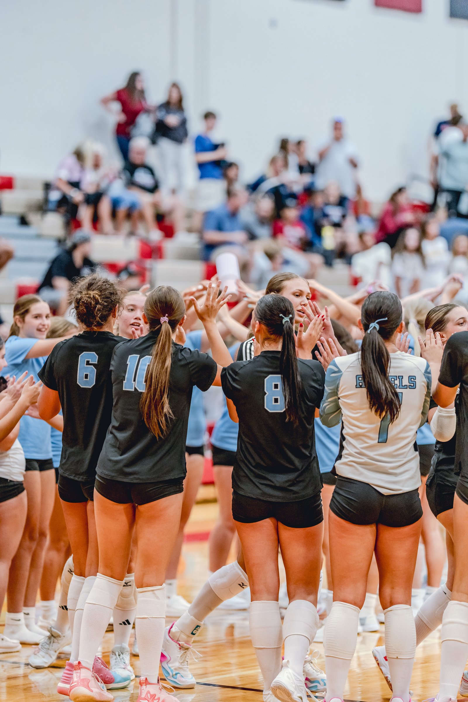 Players in black and light blue jerseys huddle together on the court, with spectators in the background.