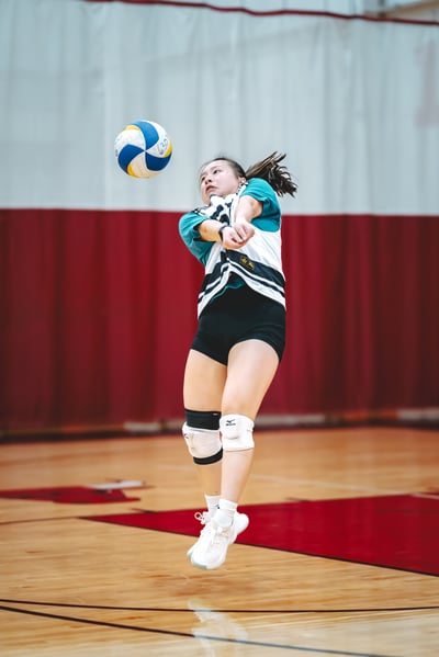 A player in a teal and white top and black shorts jumps with arms extended toward the ball.