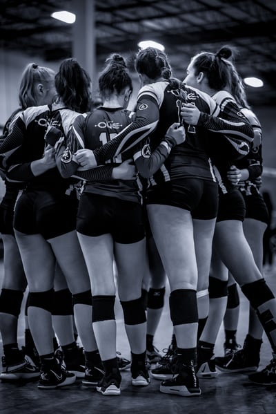 Players in black and white uniforms huddle with arms around each other on a court.
