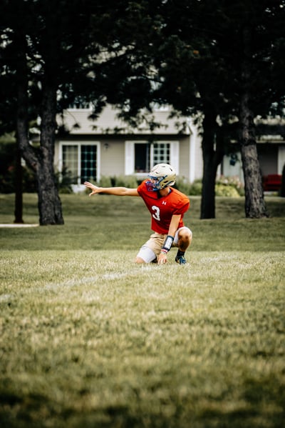 A player in red kneels on the grass with one arm extended forward.