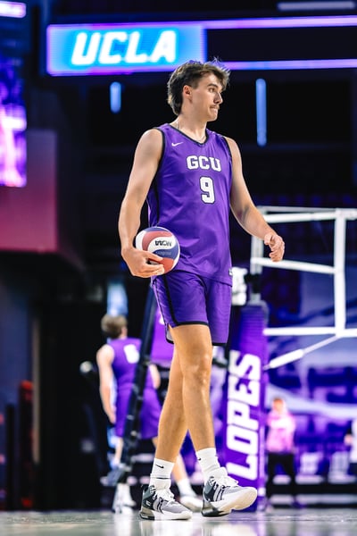 A player in purple holds a volleyball and walks forward.