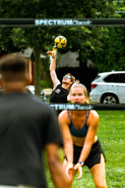 A player in black reaches up for the ball while a player in blue crouches low.