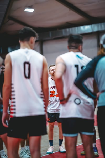 A player in white smiles while standing with hands on hips, facing players in white and black shorts.