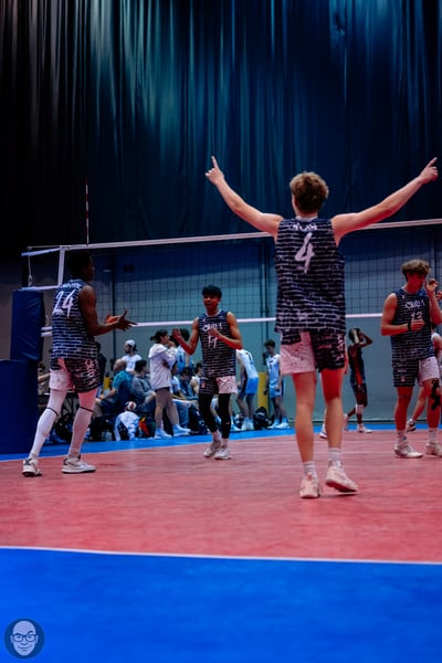 Boys volleyball players in dark blue and white jerseys celebrate a point on the court.