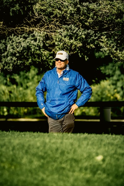 A person in a blue jacket and gray pants stands with hands on hips.