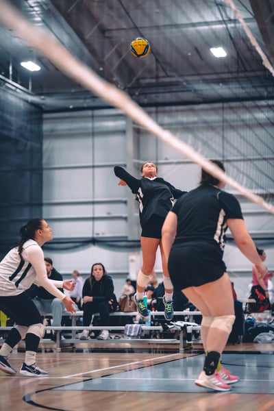 A player in black jumps for the ball while a player in white crouches.