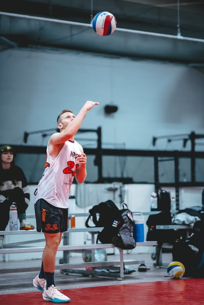 A player in a white jersey and black shorts reaches up for the ball.