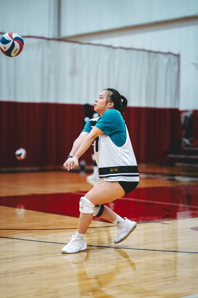 A player in a white and teal jersey crouches with arms extended toward the ball.