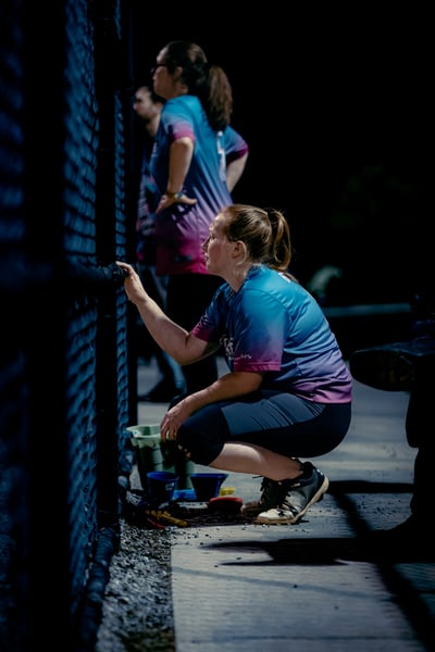 A player in a blue and pink shirt crouches and touches a fence.