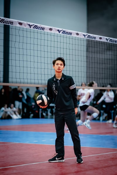 A player in black stands holding a volleyball with their left hand.
