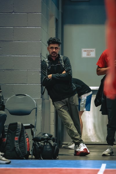 A person in a black jacket leans against a wall with arms crossed.