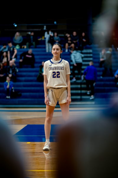A player in white shorts and a white jersey stands with her hands at her sides on a basketball court.