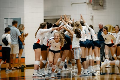 A player in white and orange jumps into a huddle with teammates.