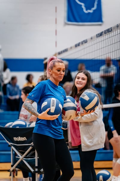 A player in a blue shirt holds three volleyballs.
