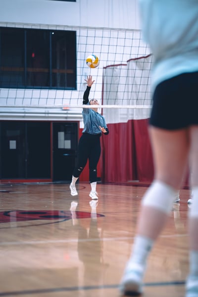 A player in gray reaches overhead for the ball while jumping on a court.