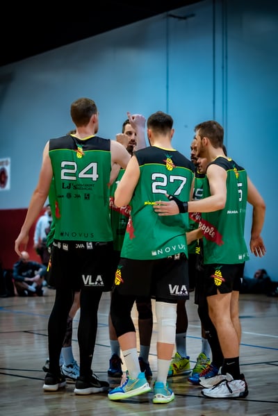 Players in green jerseys huddle together with arms around each other on a court.