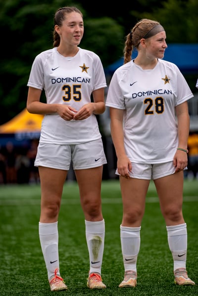 Two players in white uniforms stand on a green field, looking to the side.