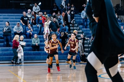 Two players in maroon uniforms run forward on a wooden court.