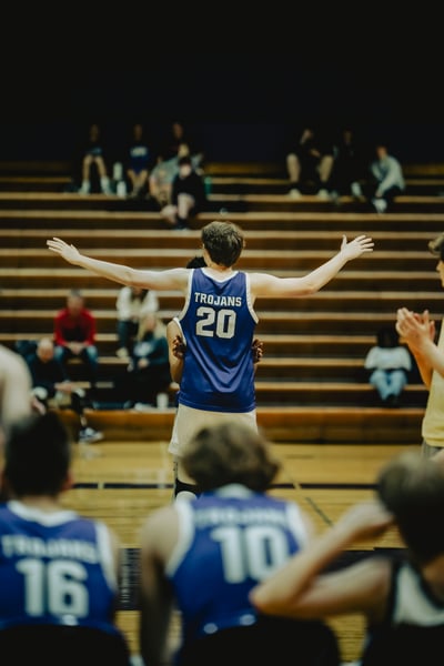 A player in a blue jersey with arms outstretched stands with another player behind them.