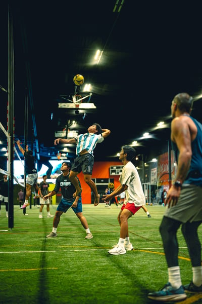 A player in a striped shirt jumps high for the ball while another player in blue shorts crouches.