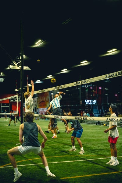 A player in white jumps toward the ball while a player in blue and white stripes leaps to hit the ball.