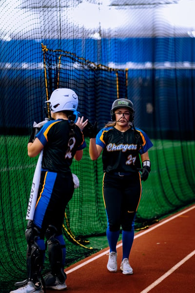 A player in black and blue high-fives a player in black and blue while holding a bat.