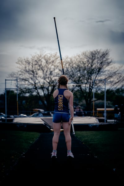 A player in blue shorts and a blue top holds a pole vertically with both hands.