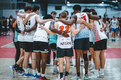 Players in white and blue jerseys huddle together with arms around each other on a basketball court.