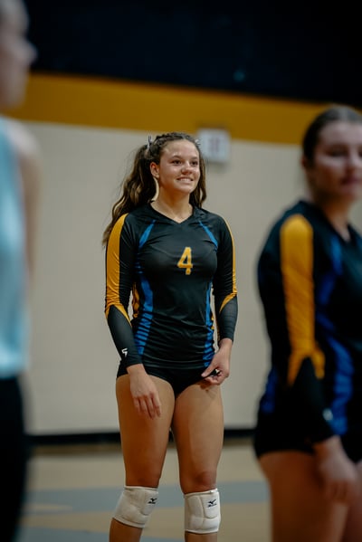 A player in a black and gold uniform stands with hands at her sides.