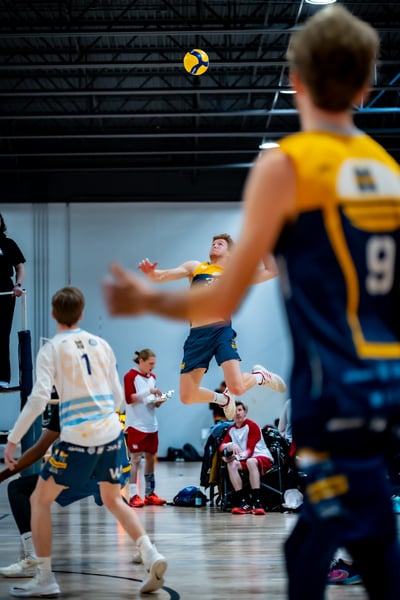 A player in blue shorts and a yellow and blue top jumps in the air towards the ball.