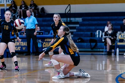 A player in a black and yellow uniform crouches low with arms extended.