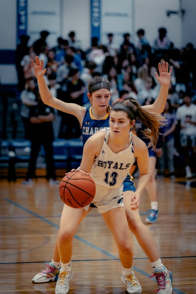 A player in white dribbles the ball while a player in blue defends.