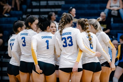 A team in white huddles together with arms around each other.