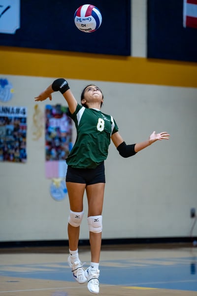 A player in green jumps with arms extended toward the ball.