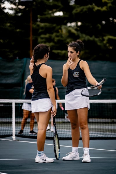 A player in a black top and white skirt holds a tennis racket.