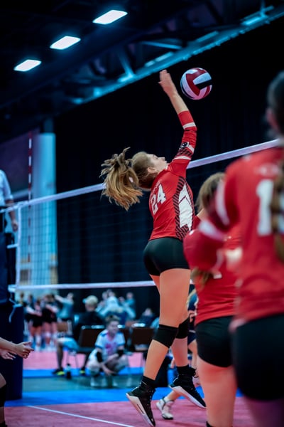 A player in red jumps and reaches overhead for the ball.