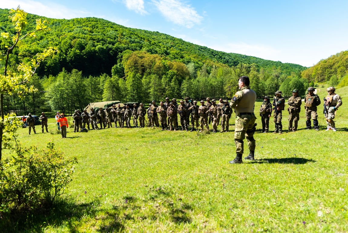 Membrii echipei Airsoft DTS în formație tactică în timpul unei operațiuni în pădure, purtând echipamente de camuflaj și echipament de stil militar