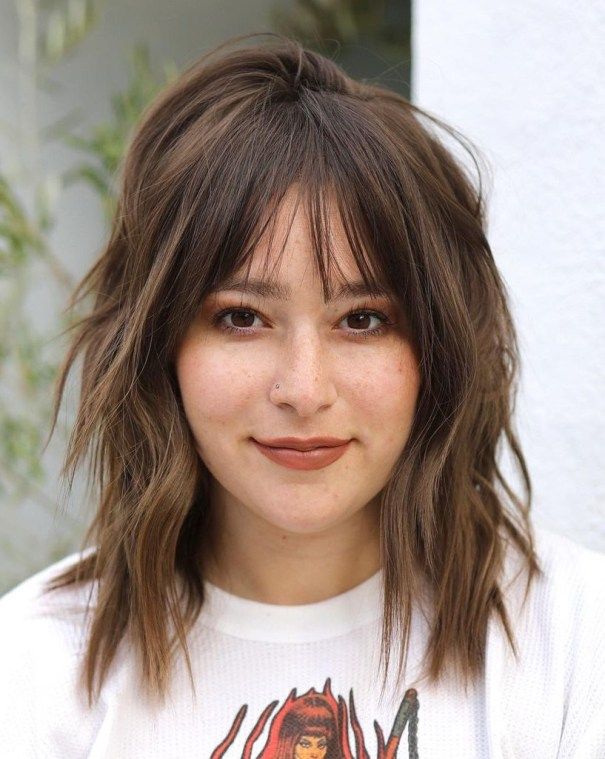 the image shows, mid length shag haircut with straight bangs