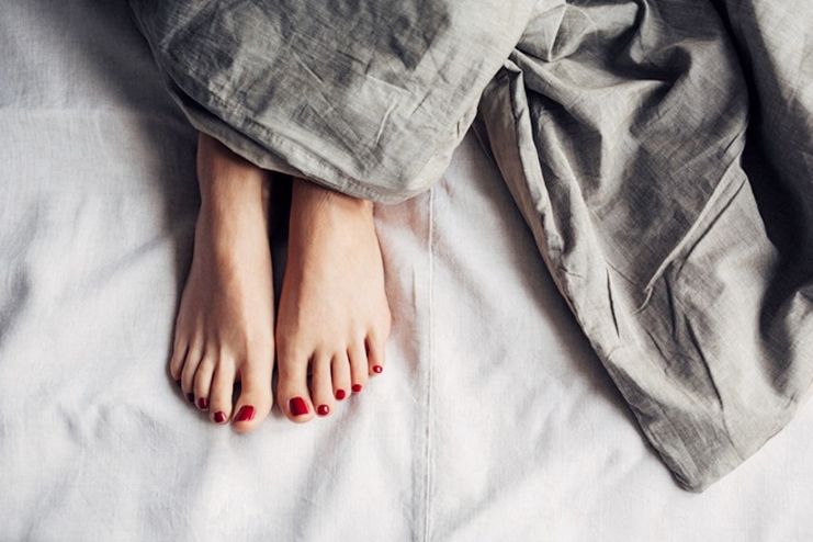 In this image show, the simple red color foot nails design pose with using the bedsheet.
