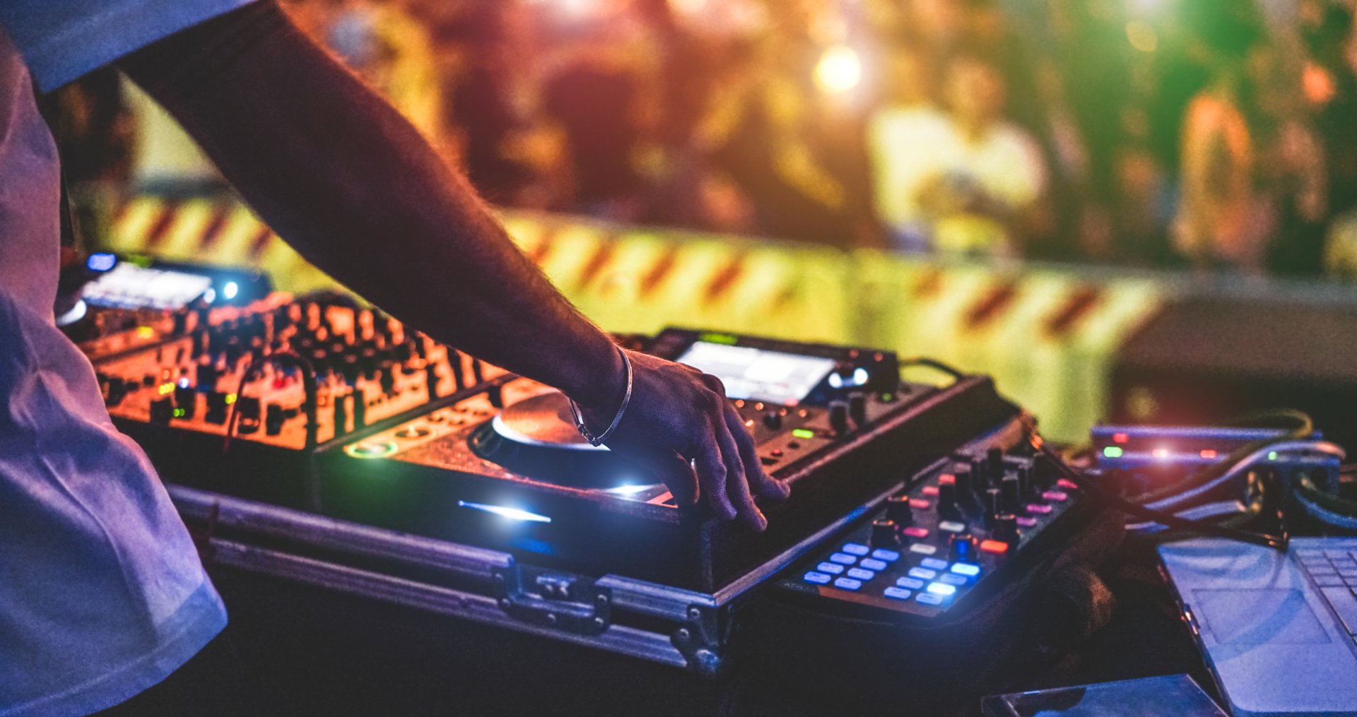 DJ wearing headphones mixes music on a console, colorful lights and fog create a vibrant atmosphere in a dimly lit room.