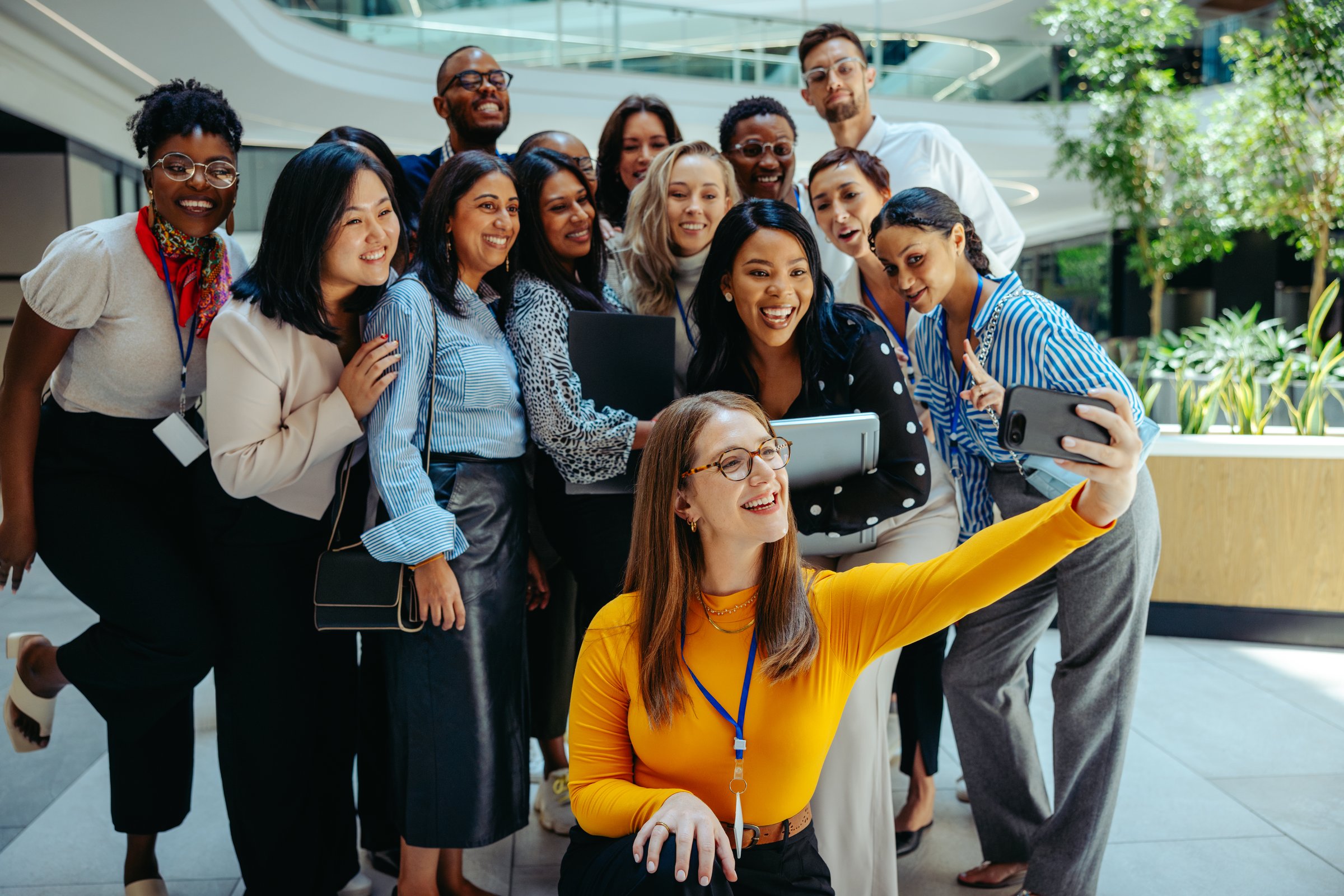 A diverse group of coworkers at an auditing firm take a joyful group selfie to welcome the new team members on their first day. The image captures a sense of excitement, camaraderie, and inclusiveness.