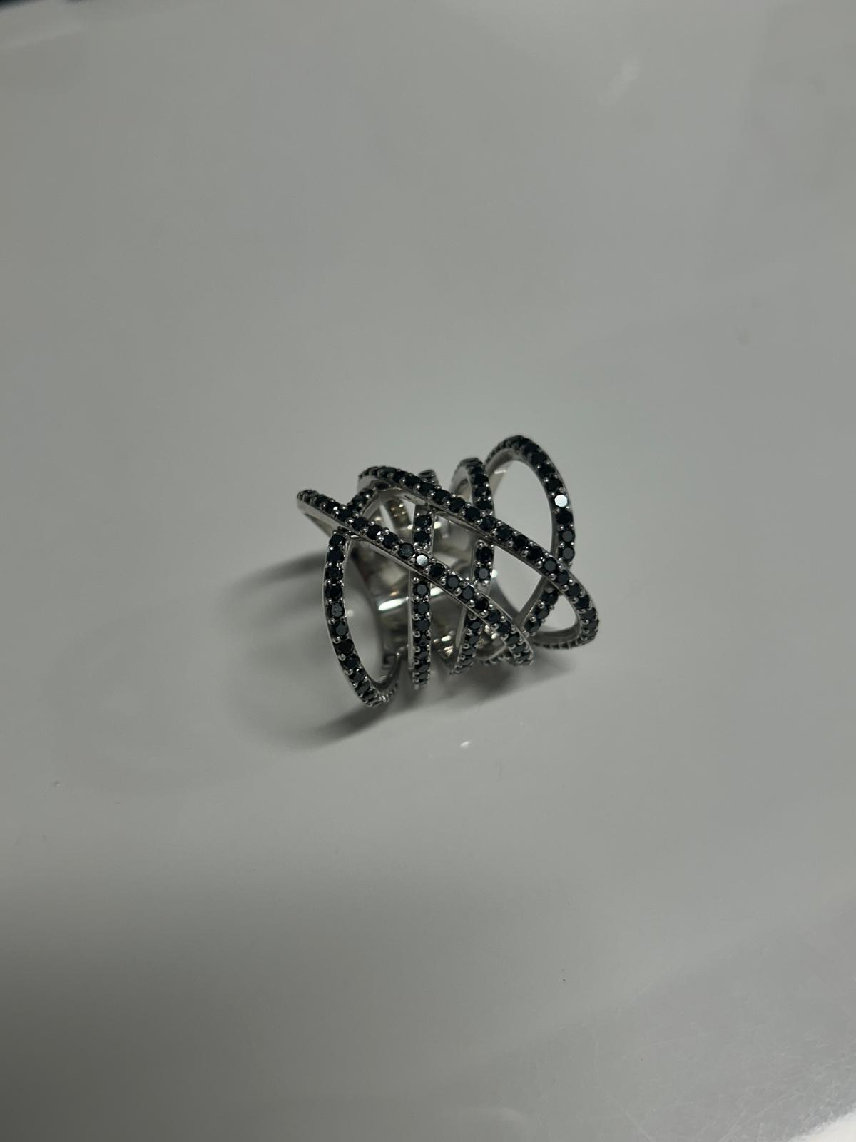 Silver ring with intertwined loops and small black gemstones on a white background.
